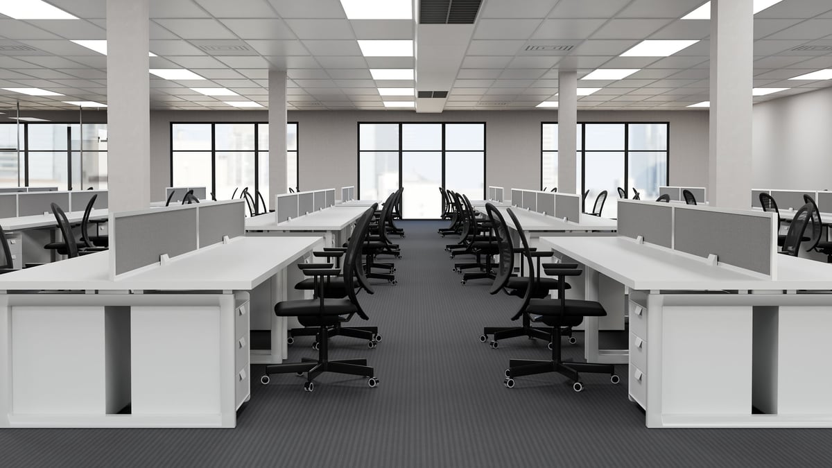 A bright, empty open-plan office with rows of clean white workstations and black chairs